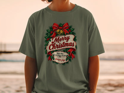 Olive green t-shirt with a Christmas wreath graphic, red bow, bells, and text.