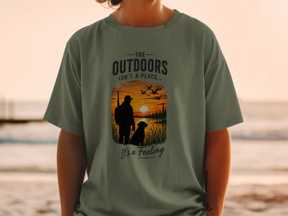 T-shirt with graphic: hunter, dog, sunset over lake, and text "The Outdoors Isn't a Place... It's a Feeling"