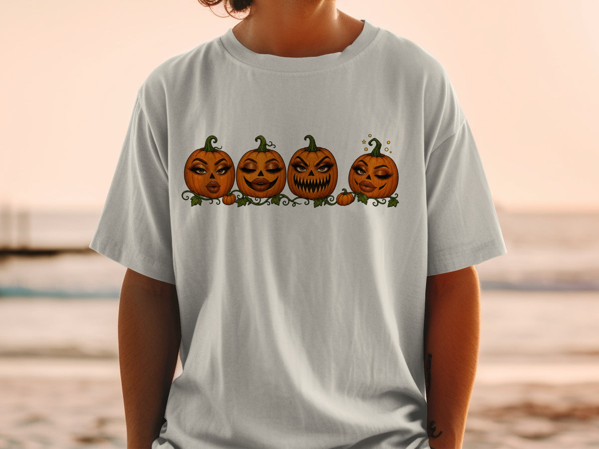Four cartoon pumpkins with glamorous makeup and leafy vines printed on a gray t-shirt.
