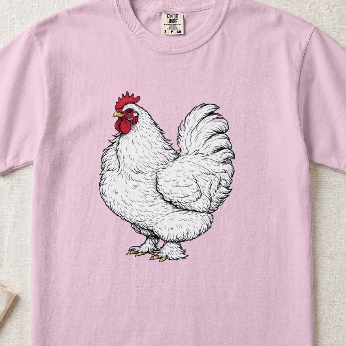A light pink t-shirt featuring a detailed illustration of a fluffy white rooster with a red comb.