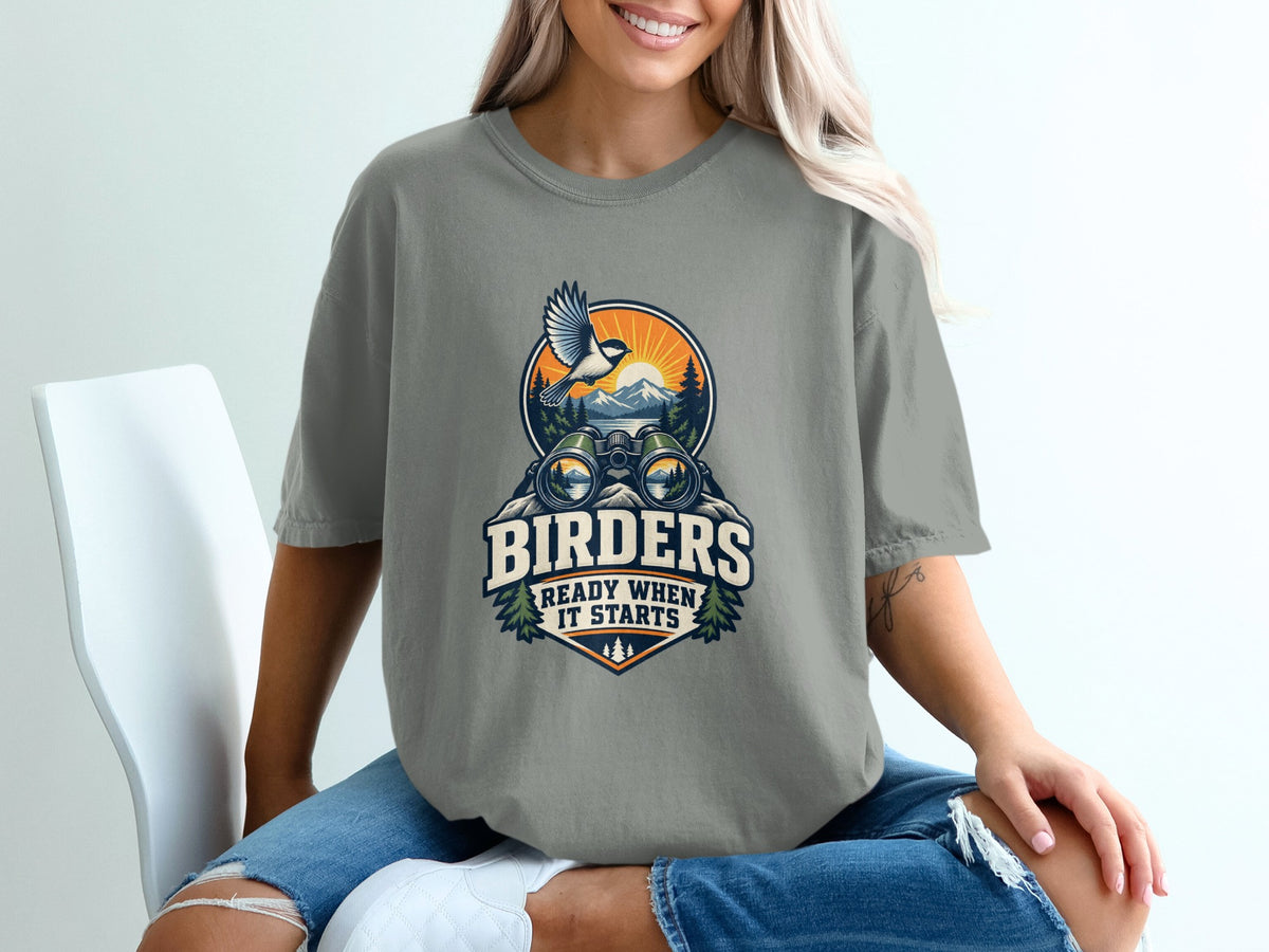 Graphic on t-shirt with binoculars, bird, mountains, sun, and text "BIRDERS READY WHEN IT STARTS".