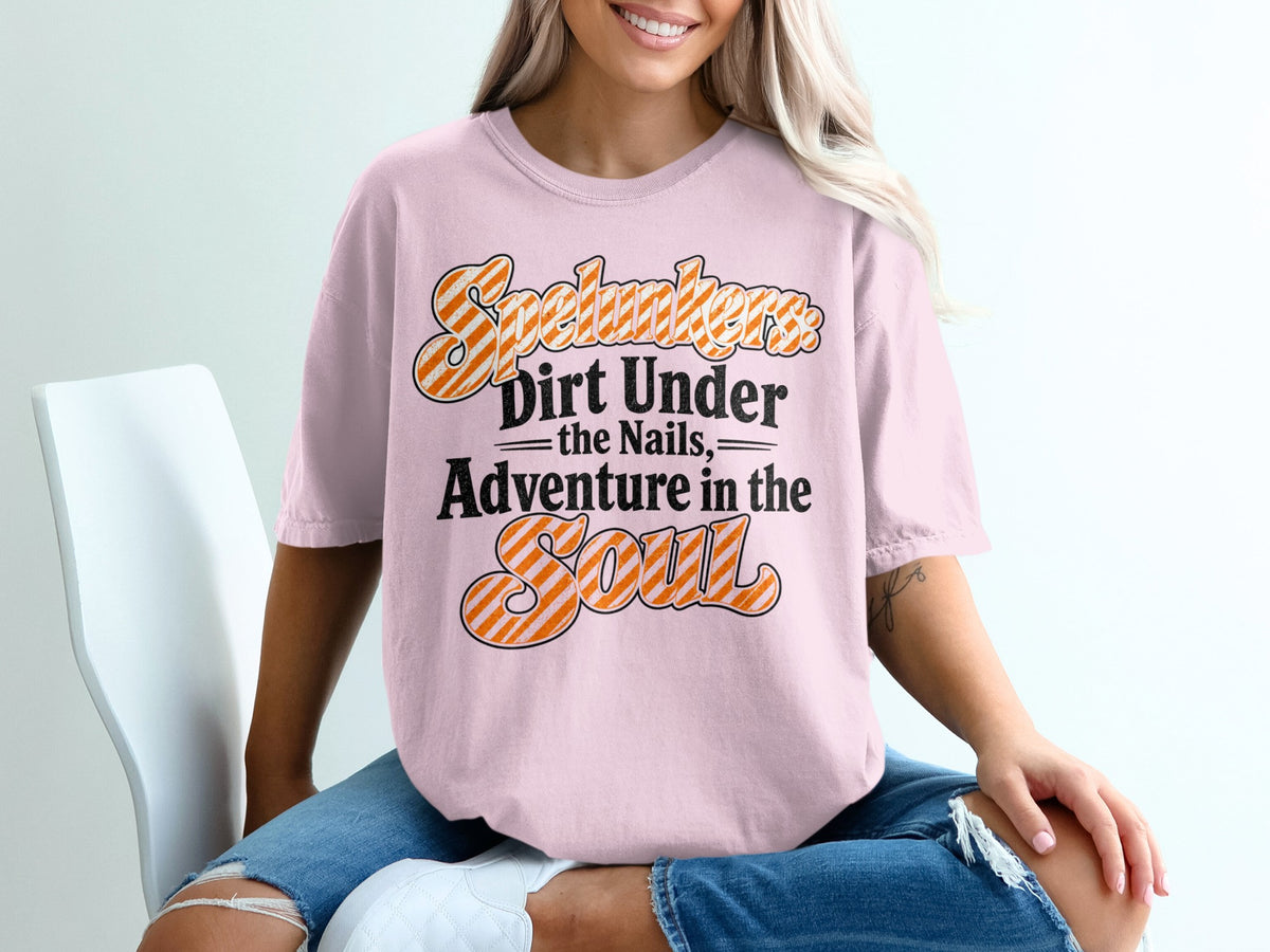 Pink t-shirt with orange and white striped text: "Spelunkers Dirt Under the Nails, Adventure in the Soul".