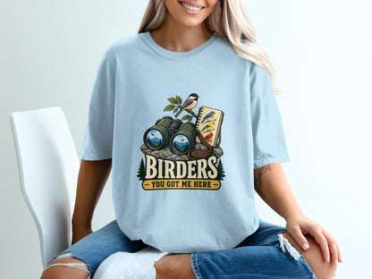 Light blue t-shirt with a graphic of binoculars, birds, and the text "BIRDERS YOU GOT ME HERE".