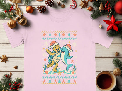 Pink t-shirt with a holiday graphic of a happy turtle and dolphin hugging.