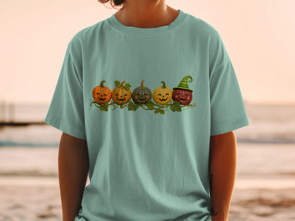Five smiling pumpkins, one wearing a witch hat, on a vine across a green t-shirt.