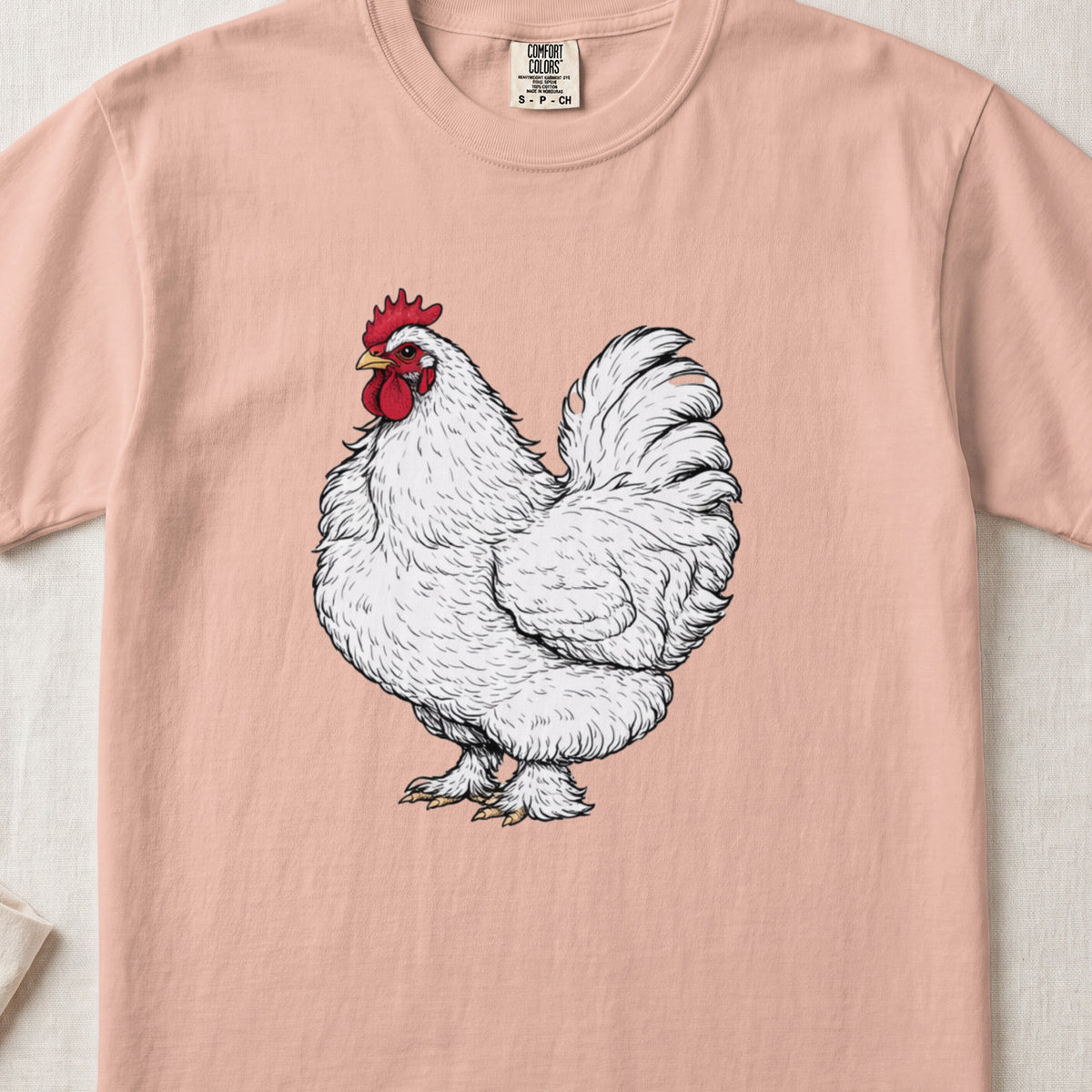 A peach-colored t-shirt featuring a detailed illustration of a white rooster centered on the chest.