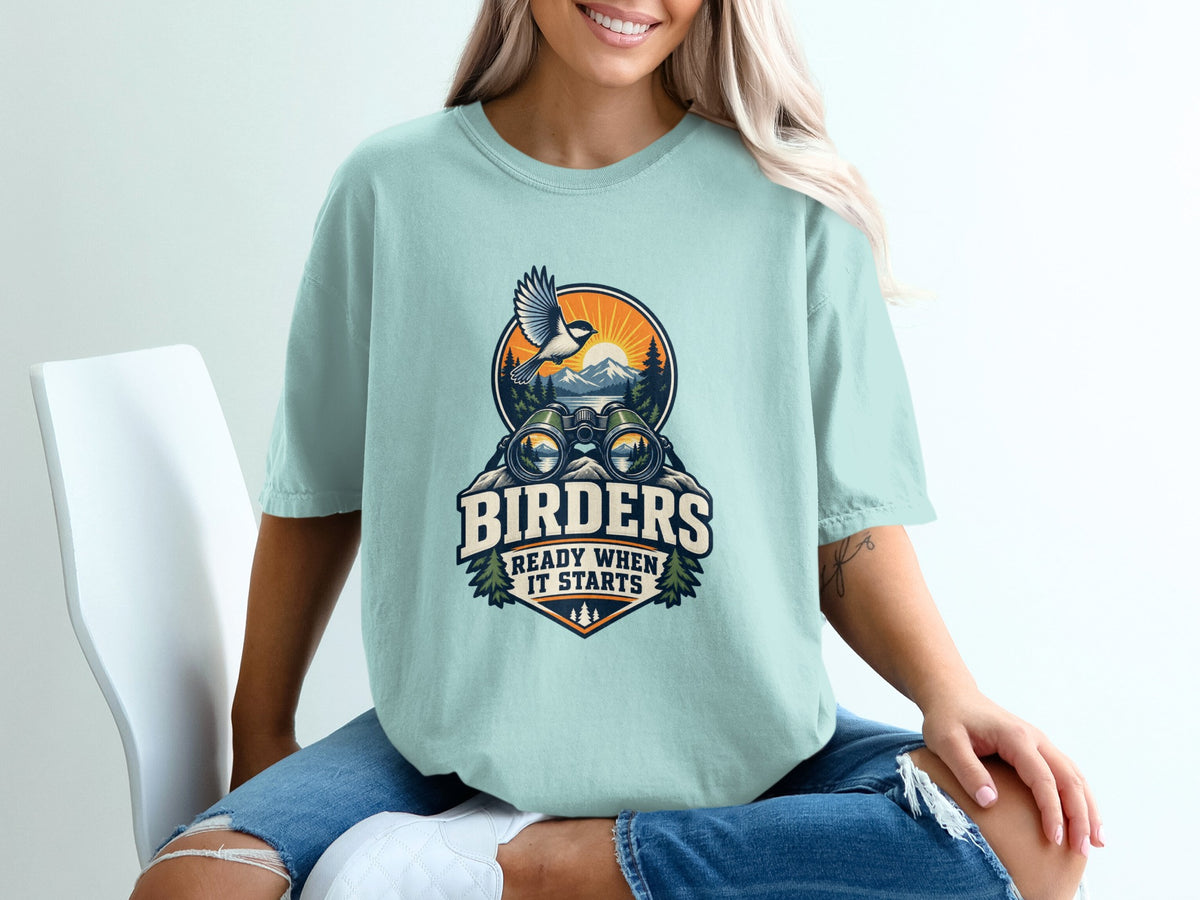 Light blue t-shirt with graphic design of binoculars, a bird, and text "BIRDERS READY WHEN IT STARTS".