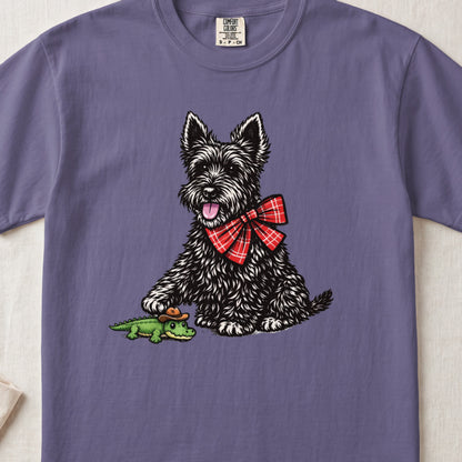 A purple t-shirt featuring a graphic of a black terrier wearing a red plaid bow tie, touching a toy alligator.
