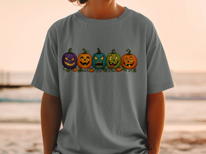 Five cartoon Halloween pumpkins with different facial expressions on a dark gray t-shirt.