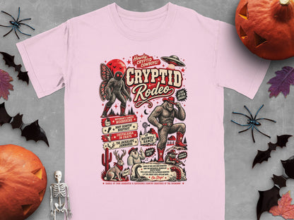 Pink t-shirt with "Cryptid Rodeo" graphic featuring Bigfoot, Mothman, and other cryptids.