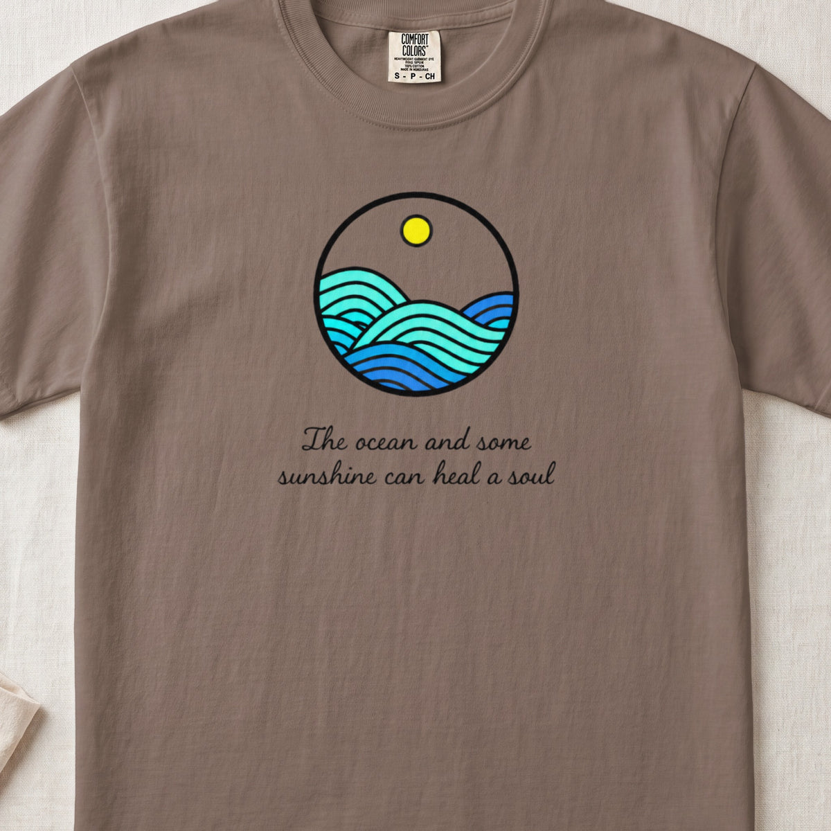 Brown t-shirt featuring a circular ocean graphic with a yellow sun and text reading The ocean and some sunshine can heal a soul.