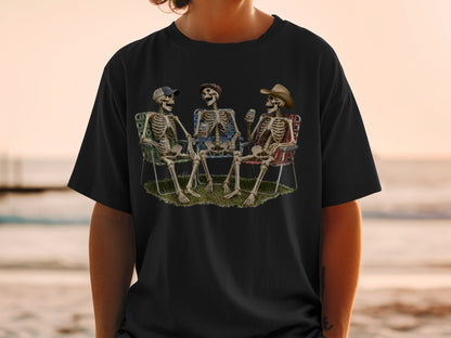 Three skeletons wearing hats relax in lawn chairs on grass, holding drinks.