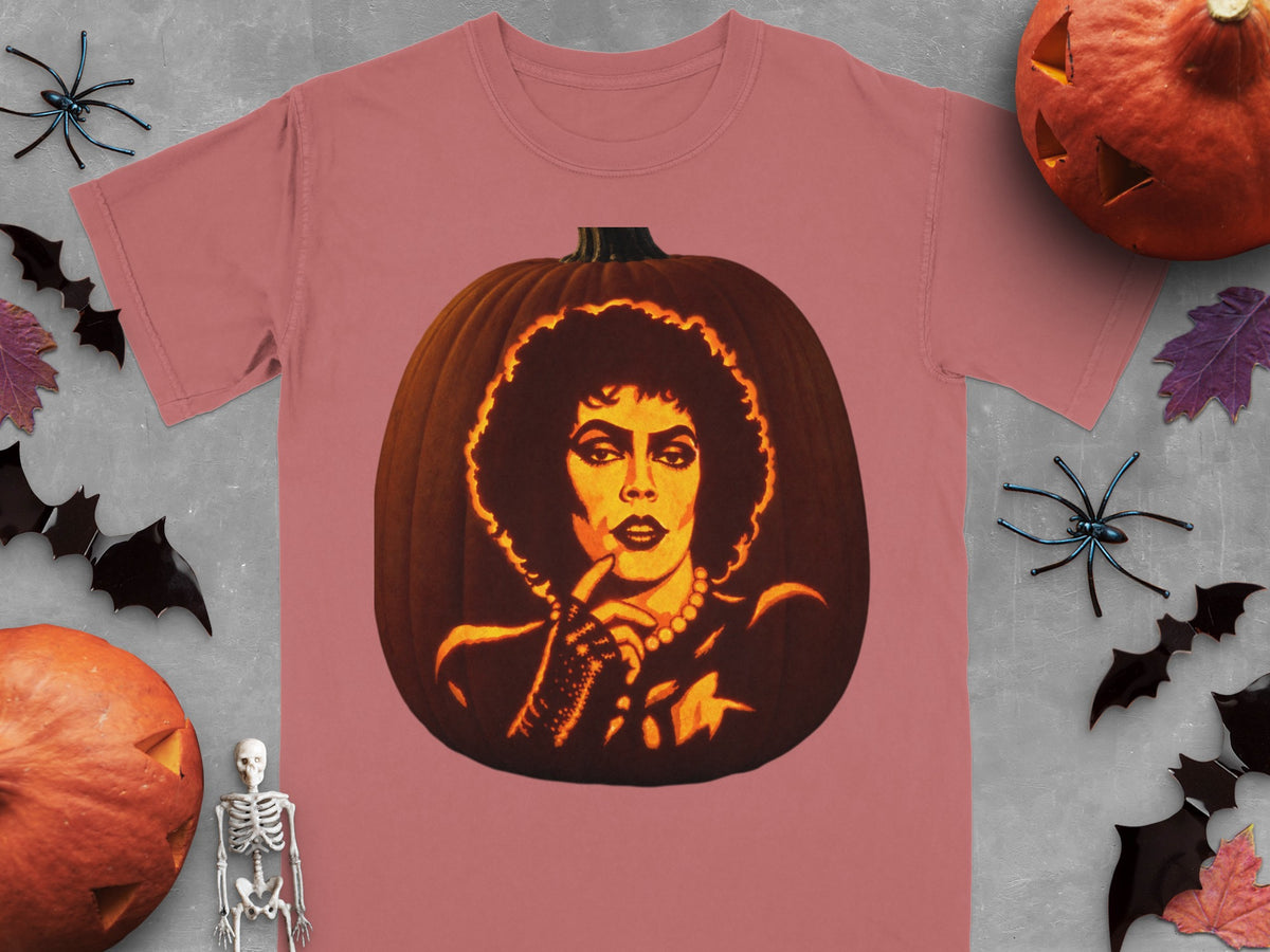 A mauve t-shirt featuring a carved pumpkin graphic of Frank-N-Furter, surrounded by Halloween decor on a gray background.