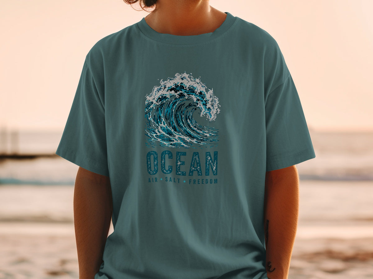 Teal t-shirt with a large blue wave graphic and text "OCEAN AIR SALT FREEDOM".