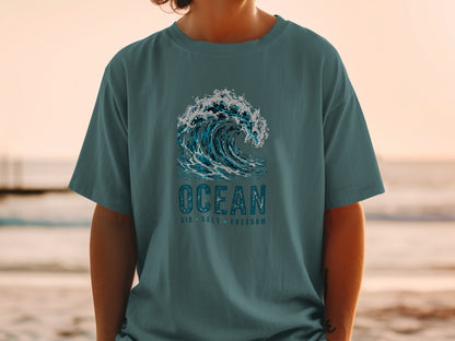 Teal t-shirt with a large blue wave graphic and text "OCEAN AIR SALT FREEDOM".