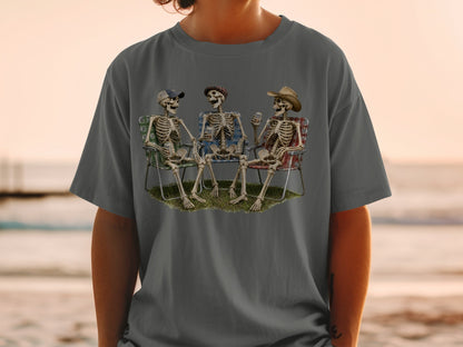Three skeletons wearing hats relax in lawn chairs holding drinks.