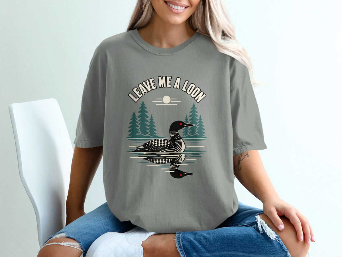 T-shirt graphic with text "Leave Me a Loon", loon on water, trees, and sun.